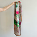 Silk scarf with floral design held by a hand against a plain background