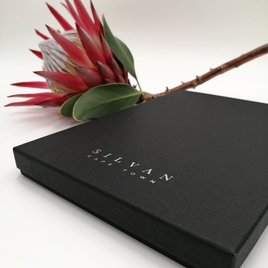 A black scarf box with silver foiled embossed branding.